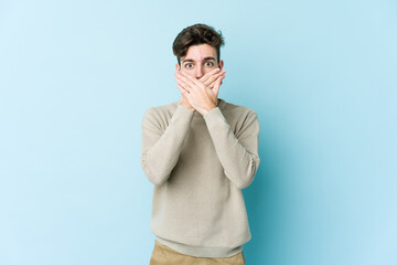 Young caucasian man isolated on blue background shocked covering mouth with hands.