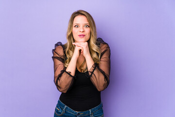 Young caucasian woman isolated on purple background praying for luck, amazed and opening mouth looking to front.