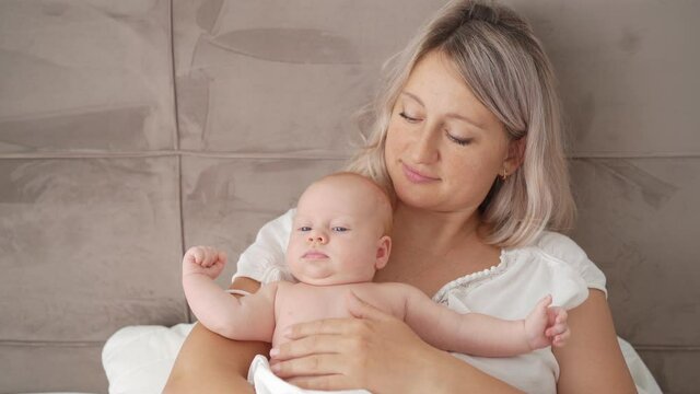 mom sits with baby in bed and kisses. concept of maternal love, newborn care.
