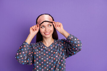 Photo of positive cheerful girl touch hand eye mask look copyspace wear dotted pajama isolated over purple violet color background