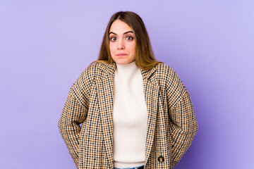 Young caucasian woman isolated on purple background shrugs shoulders and open eyes confused.