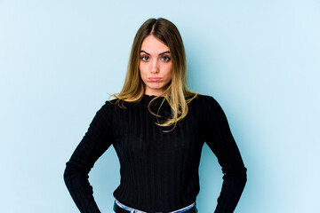 Young caucasian woman isolated on blue background blows cheeks, has tired expression. Facial expression concept.