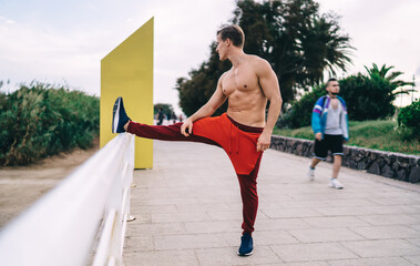 Strong male trainer 20s stretching body muscles during morning workout in city, shirtless sportsman with pumped up abs press doing exercising for keeping healthy lifestyle and feel flexible