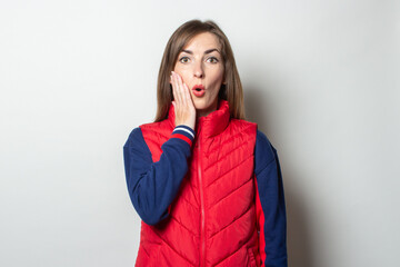 Young woman with a surprised face in a red vest on a light background