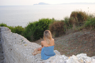 Blonde girl sitting on the rocks and looking at the sea