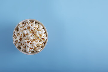 Popcorn in a plate on a blue background top view with copy space