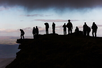 Black silhouettes of hikers on the top of a mountain resting below a grey cloud after a mountaineering ascend.