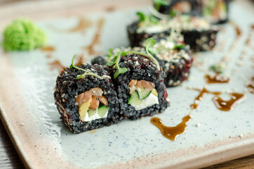Set of rolls of black rice, fish and philadelphia cream cheese, sesame seeds, on a white plate, poured with unagi sauce and microgreen sprouts, side view