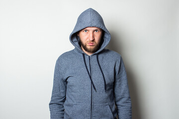 Young man in a hood with a serious, aggressive face on a light background