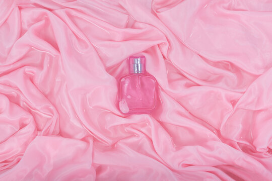 Transparent Glass Cosmetic Perfume Bottle In Folds Of Pink Cloth In Water. View From Above.