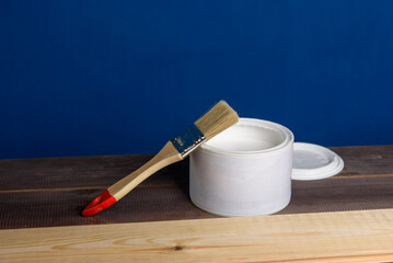 A can of white paint and a paintbrush on a wooden table