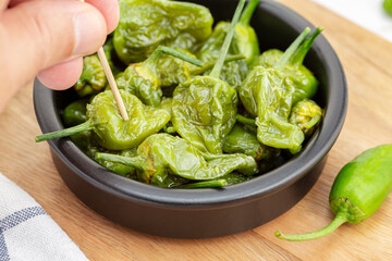 Hand picking a Cooked Padron peppers in a a bowl. Traditional Spanish appetizer
