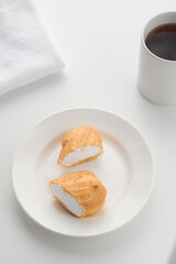 The custard cut eclair cake lies on a white plate with a glass on the background. Photography in a light key