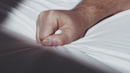 Close up of male hand grasping the bedsheet while reaching climax during sex