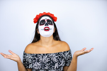 Woman wearing day of the dead costume over isolated white background clueless and confused expression with arms and hands raised