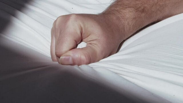 Close up of male hand grasping the bedsheet while reaching climax during sex
