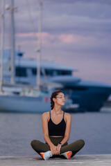 Fototapeta na wymiar Athlete girl sitting by the sea in a port with boats. She wears sports clothes and the girl is a brunette with an athletic body. She is relaxed contemplating the ocean
