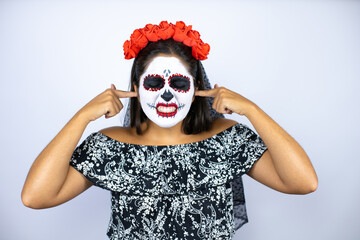 Woman wearing day of the dead costume over isolated white background covering ears with fingers with annoyed expression for the noise of loud music. Deaf concept.
