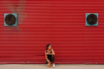 Runner rests leaning against a red wall. Athlete girl with sportswear next to her water bottle on the street