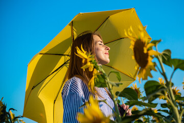 Young woman in dress and yellow umbrella on a field of sunflowers
