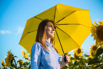 Young woman in dress and yellow umbrella on a field of sunflowers