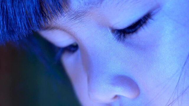Close up of little girl in bed looking at the smartphone at night and the blue light has a negative effect on children's eyes.