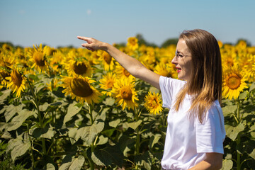Young woman in white t-shirt and glasses points with a finger on a sunflower field on a summer sunny day