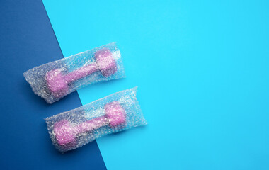 a pair of sports purple dumbbells in a transparent bag on a blue background, top view