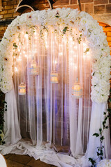 Wedding ceremony with a vintage candles. Arch for wedding area a is decorated with white flowers and greenery.