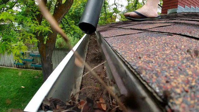 A leaf blower is seen blowing leaves and debris out of a rain gutter on a roof in slow motion.