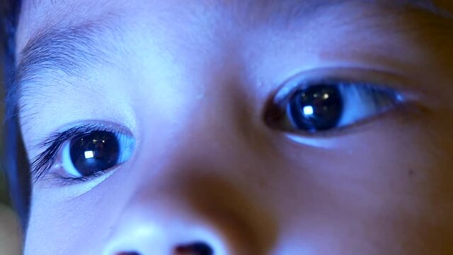 Close up of little girl in bed looking at the smartphone at night and the blue light has a negative effect on children's eyes.