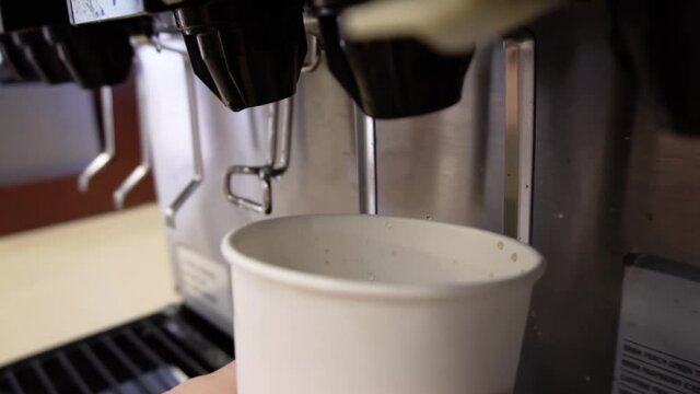 Soda dispenser machine filling a white paper cup with black, cola flavored fizzy liquid