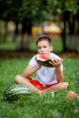 12 year old boy in white t-shirt eating watermelon on the grass in the park