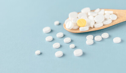 White tablets and one yellow on a wooden spoon on blue background.