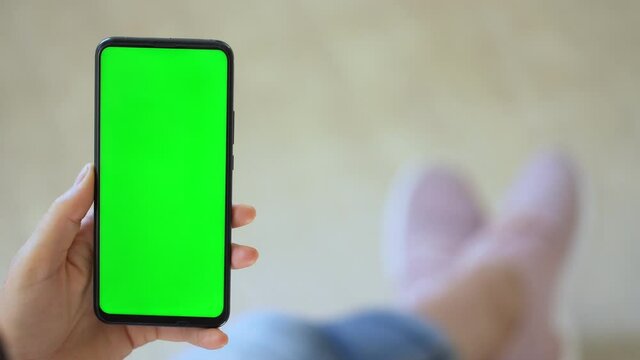 Handheld Camera: Back view of brunette holding chroma key green screen smartphone watching content. Gadgets and contemporary people concept.