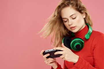 Woman with mobile set-top box headphones playing lifestyle pink background red jacket