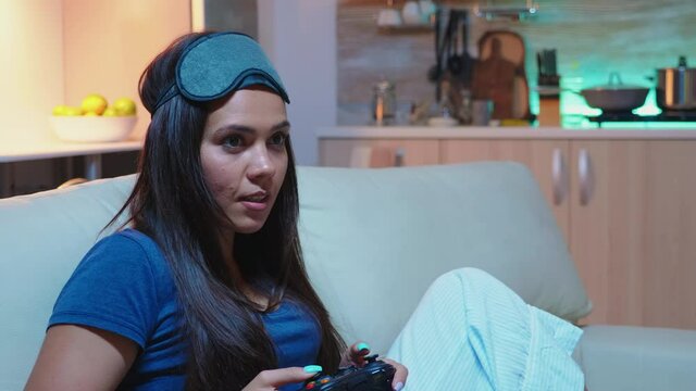 Woman addicted to computer games playing late at night on console. Excited determined gamer using controller joysticks keypad playstation gaming and having fun winning electronic game
