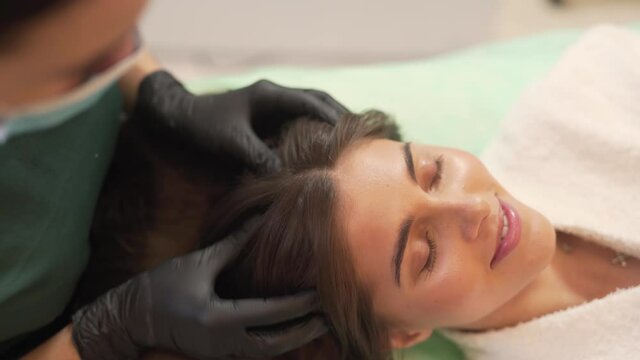 High Angle of Caucasian Female Laying Down While Her Doctor With Gloves And Mask Over Mouth Massage Her Head as Part of Hair Mesotherapy Treatment