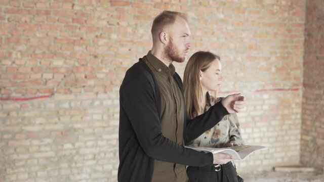 Caucasian Couple Buyers of Real Estate Property Looking at Documentation and Discuss About Rooms Arragement. Light Camera Movement