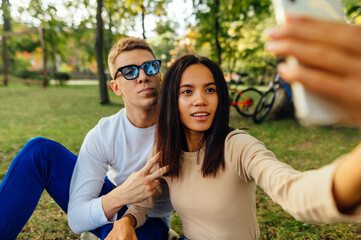 Beautiful young couple sitting on the lawn in the park and taking a selfie on a smartphone. Woman taking photo with boyfriend while relaxing in the park