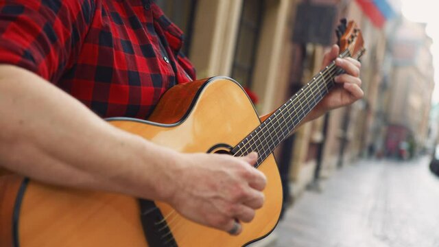Relaxed guitarist playing slow chords on the streets, close up shot