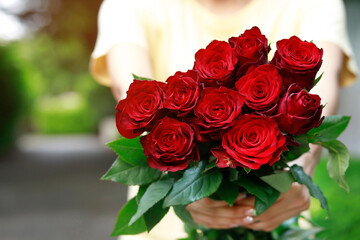close up of woman hand with red rose many flowers on outdoor background.
