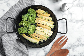 Flat lay composition with raw white carrot and broccoli in frying pan on white marble table
