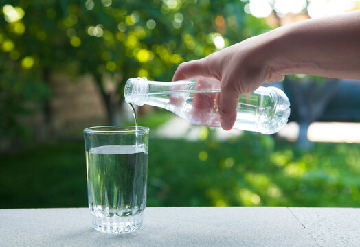 Hand Holding Drinking Water Bottle Pouring Water Into Glass  On Green Nature Background.