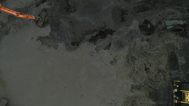 Wide aerial rising shot of machines digging a pond on a construction site. Diggers and a bulldozer moving mud.