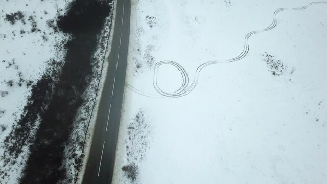 A car driving past mysterious tire tracks in snow, chilly winter landscape, drone footage, eerie feeling scene