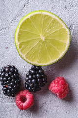 Fototapeta na wymiar Citrus lime slice, raspberry and blackberry berries, healthy summer fruits on stone concrete background, top view macro