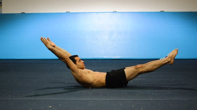 a guy doing a static hold in a gymnastics gym
working out his abs and core muscles
still shot