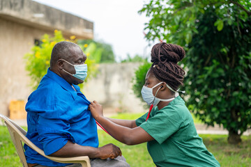 image of an aged African man being checking up by a health worker-young black nurse wearing a face...