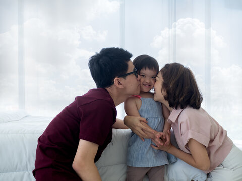 Happy family moments. Asian parents kissing  disable or down syndrome or trisomy 21 young daughter in the bedroom